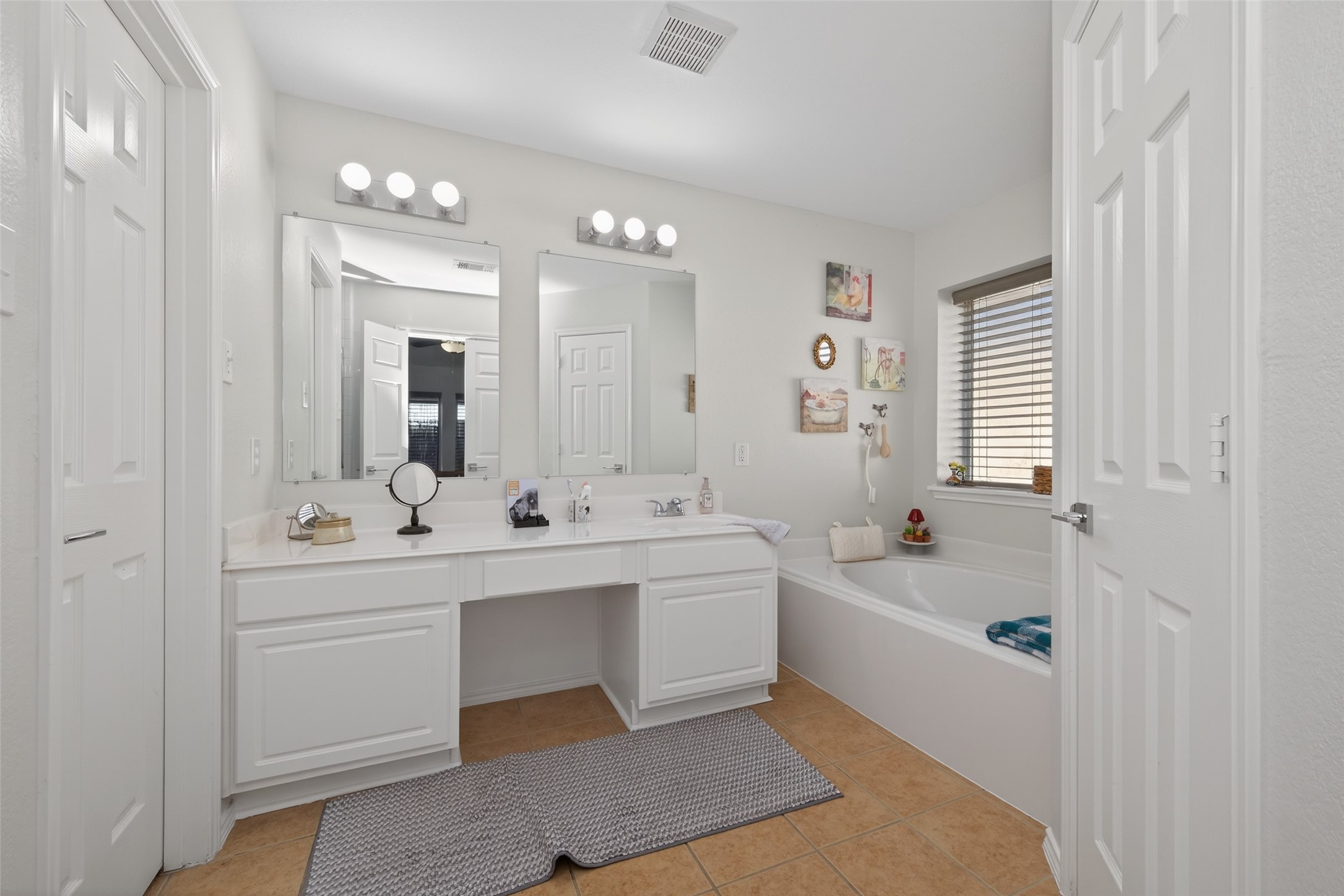 20218 Appaloosa Ridge Drive Humble, TX 77338 - Photo 32 of 44 This bathroom features a spacious dual-sink vanity with ample storage, a large mirror, and modern lighting. It includes a cozy bathtub with a window for natural light, complemented by neutral tile flooring and clean, white cabinetry.