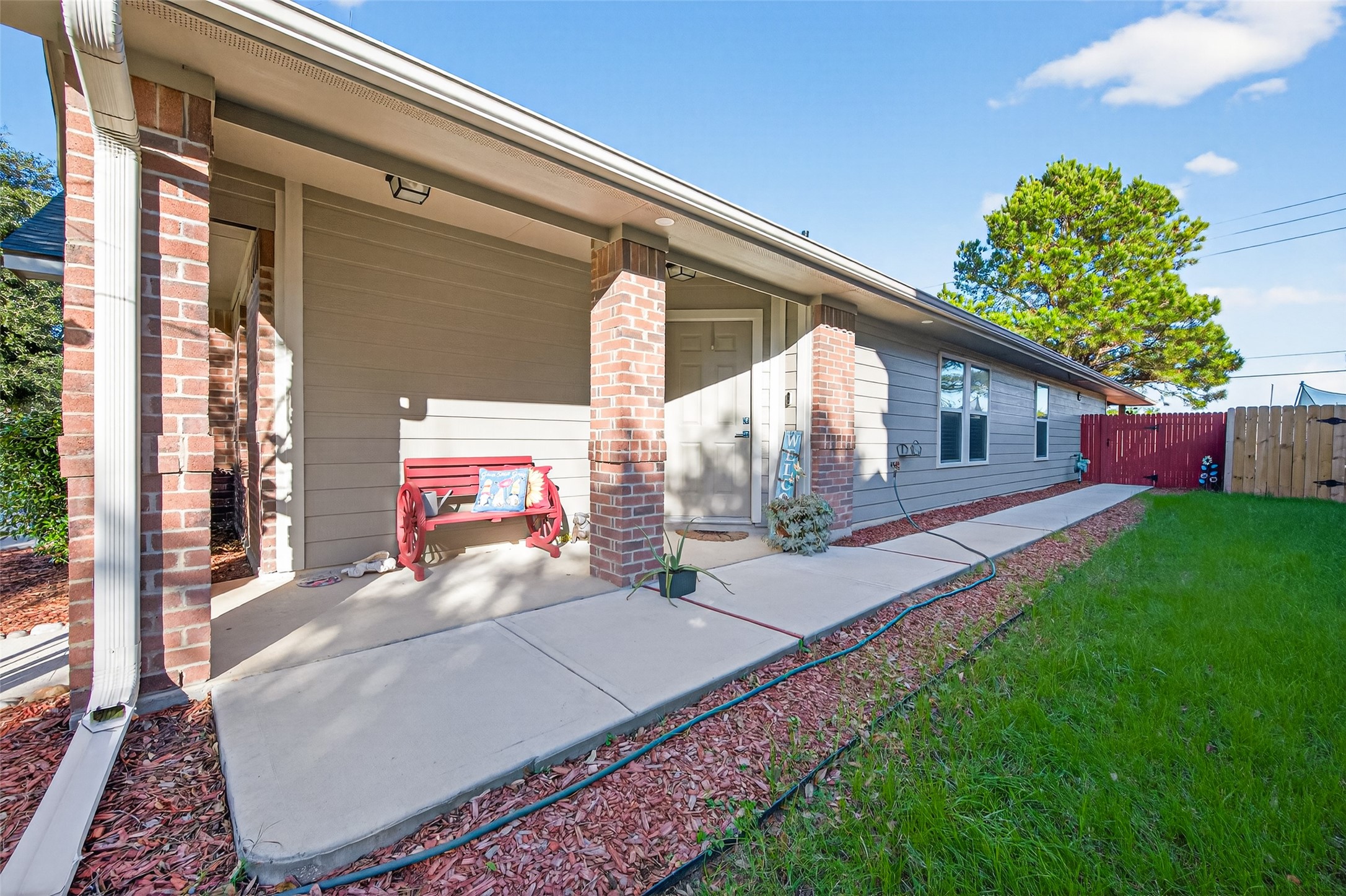 20218 Appaloosa Ridge Drive Humble, TX 77338 - Photo 36 of 44 This photo showcases a welcoming front porch with brick accents, a cozy bench, and a well-maintained walkway. The house features a manicured lawn, modern siding, and a charming red fence, offering a pleasant curb appeal.