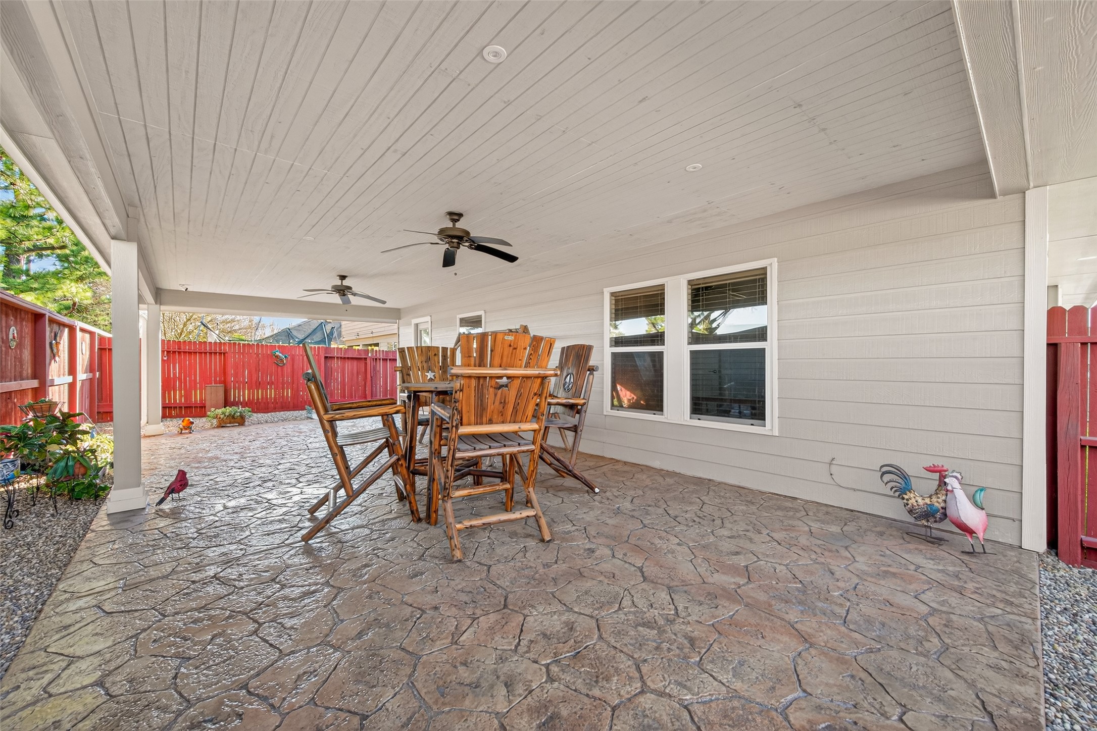 20218 Appaloosa Ridge Drive Humble, TX 77338 - Photo 37 of 44 This photo showcases a spacious covered patio with a stamped concrete floor, ceiling fans, and wooden furniture. It's perfect for outdoor gatherings, featuring a red fence and decorative accents for added charm.