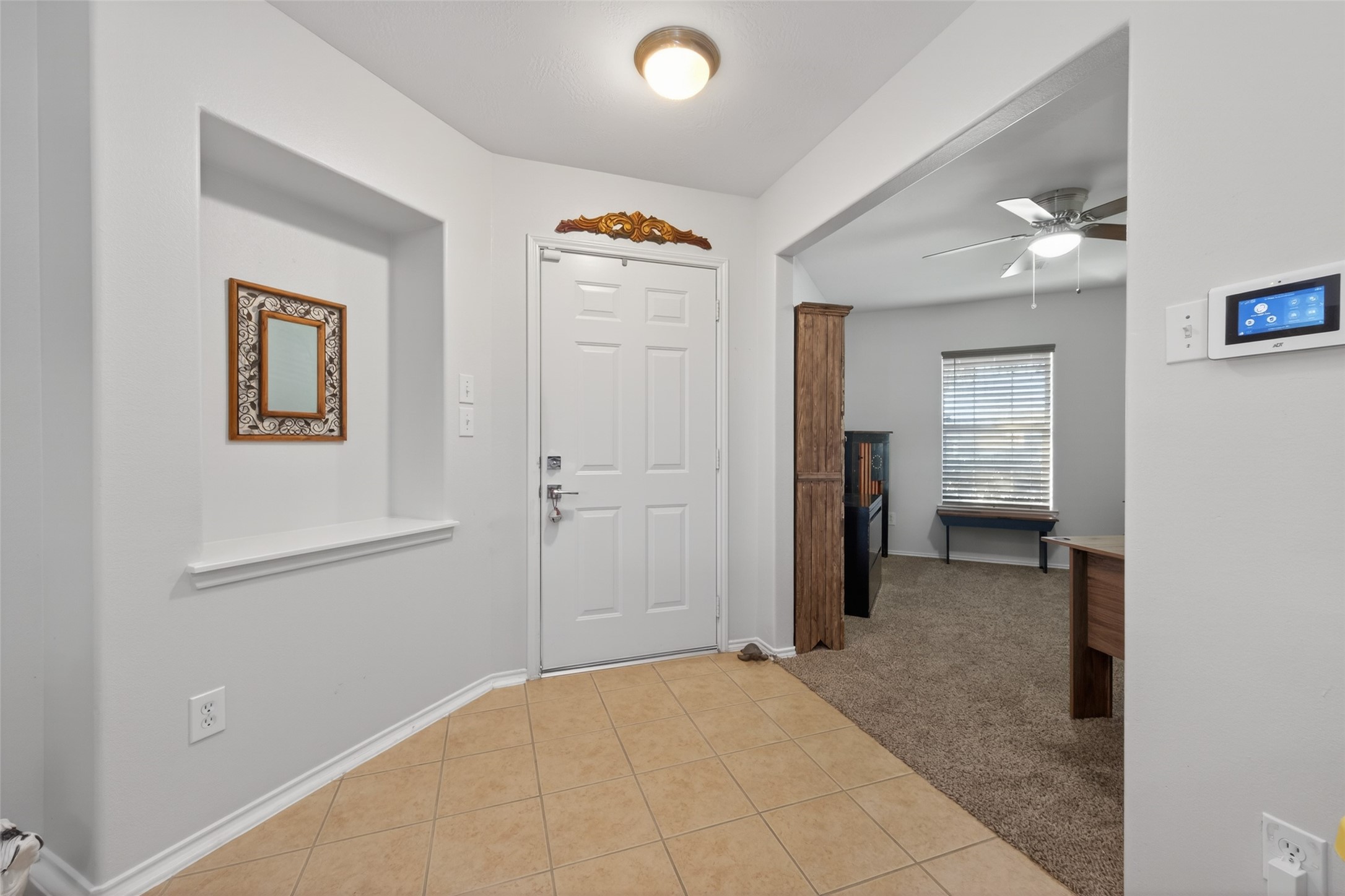 20218 Appaloosa Ridge Drive Humble, TX 77338 - Photo 8 of 44 This photo showcases a welcoming entryway with tiled flooring and a decorative niche with a mirror. It leads into a carpeted room with a ceiling fan, offering a cozy transition from the entrance.