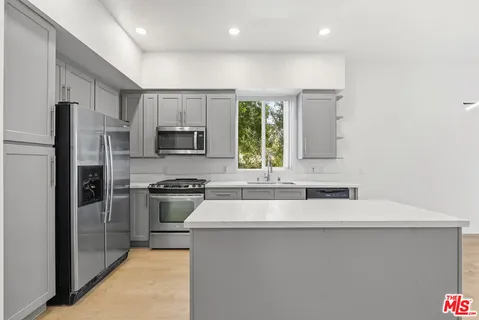 a kitchen with kitchen island granite countertop a stove a sink and a refrigerator with wooden floor