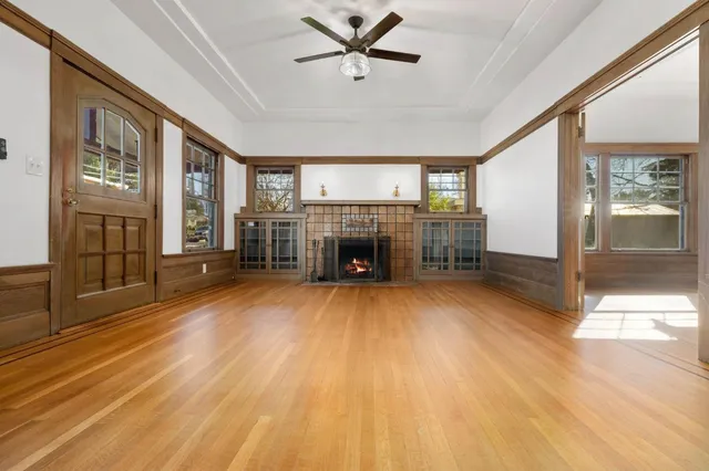 a livingroom with furniture a fireplace a ceiling fan and wooden floor