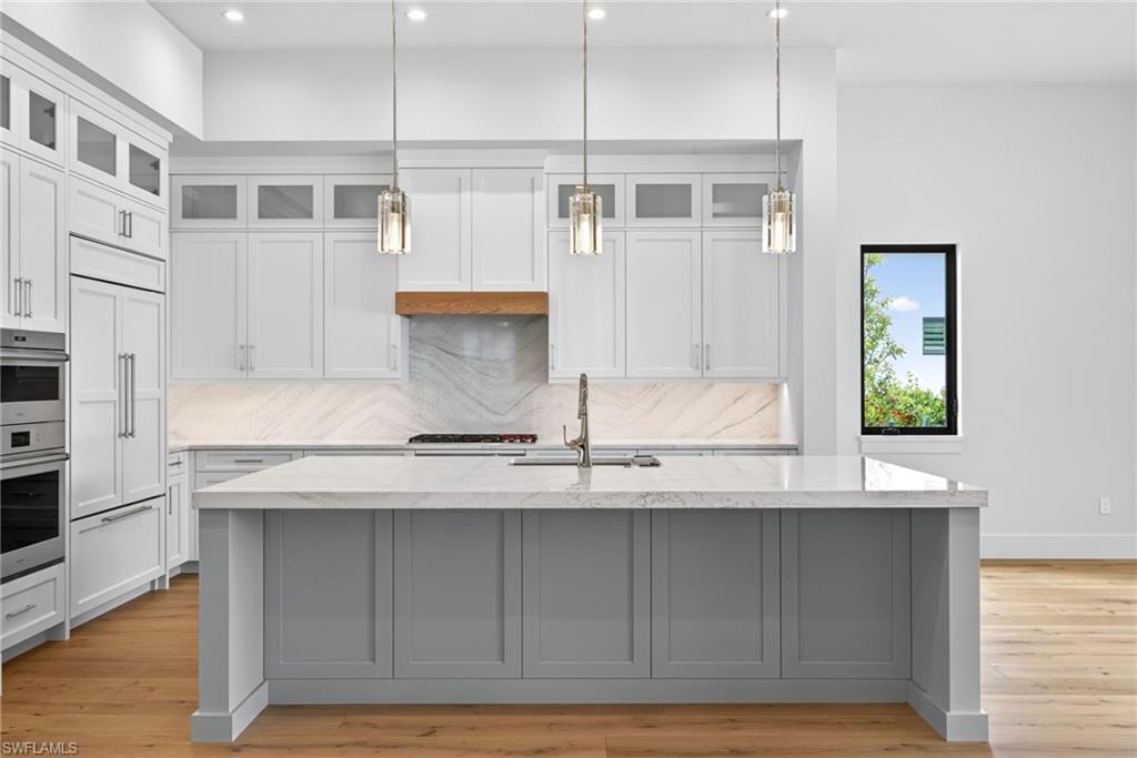 16736 Lucarno Way Naples, FL 34110 - Photo 13 of 49 Kitchen featuring glass fronted cabinets, light counters, decorative light fixtures, and wood finished floors