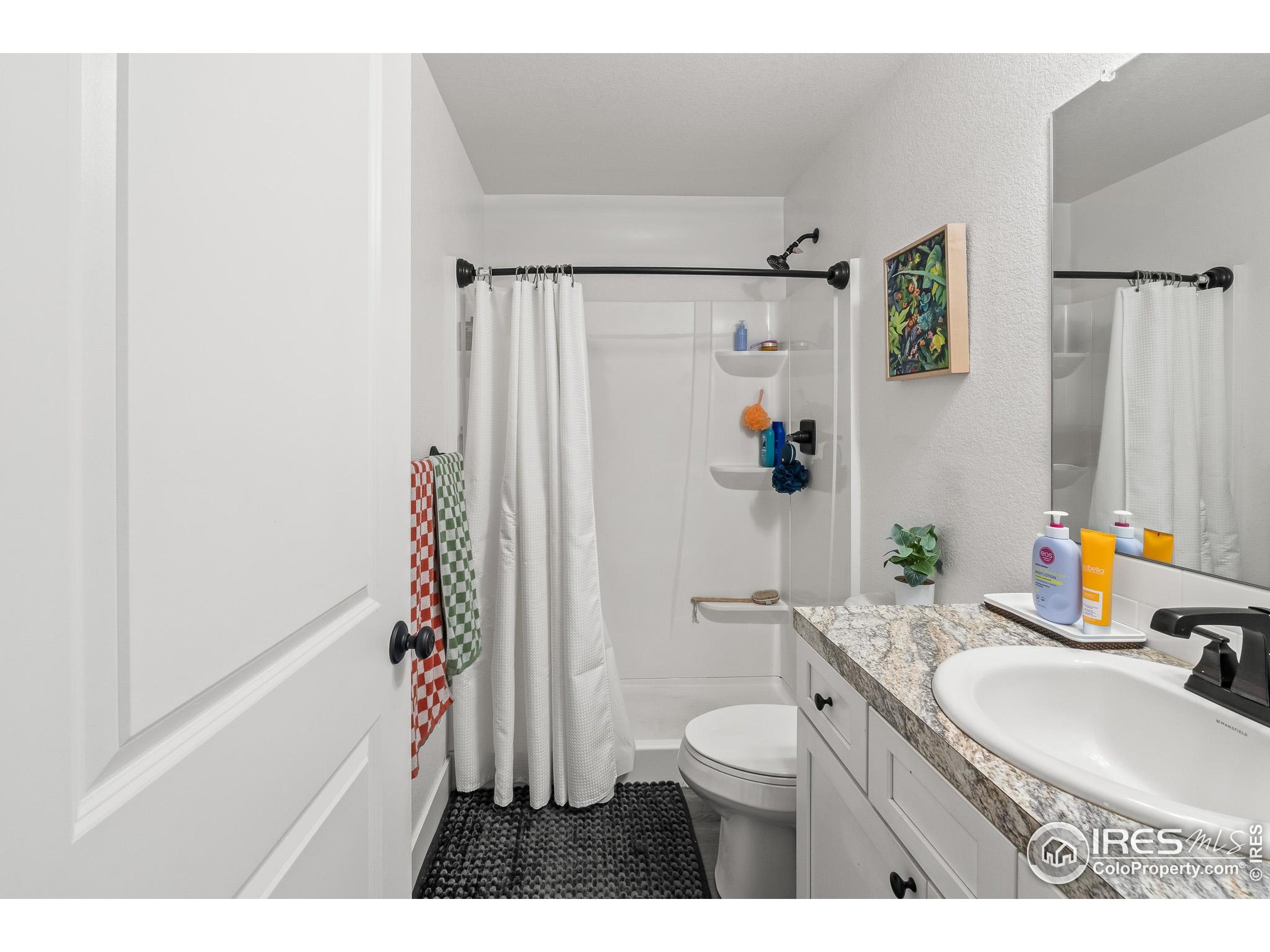2771 Red Wheat Trail Berthoud, CO 80513 - Photo 33 of 46 a bathroom with a granite countertop sink a toilet a shower curtain and a bath tub