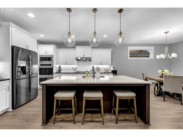 a kitchen with stainless steel appliances kitchen island granite countertop a dining table chairs sink and refrigerator