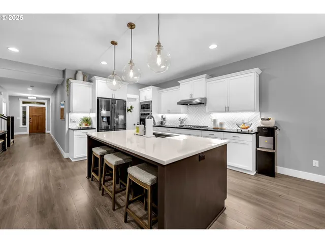 a kitchen with stainless steel appliances granite countertop a stove a refrigerator a sink dishwasher and a dining table with wooden floor