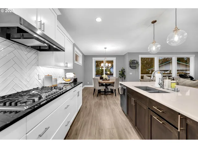 a kitchen with stainless steel appliances granite countertop a stove a sink dishwasher a dining table and chairs with wooden floor