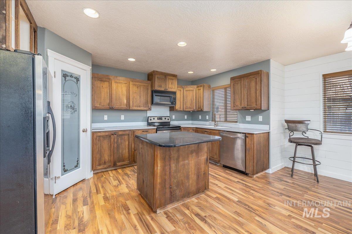 237 16th Avenue North Payette, ID 83661 - Photo 12 of 36 Kitchen featuring stainless steel appliances, brown cabinetry, a center island, a textured ceiling, and light wood finished floors