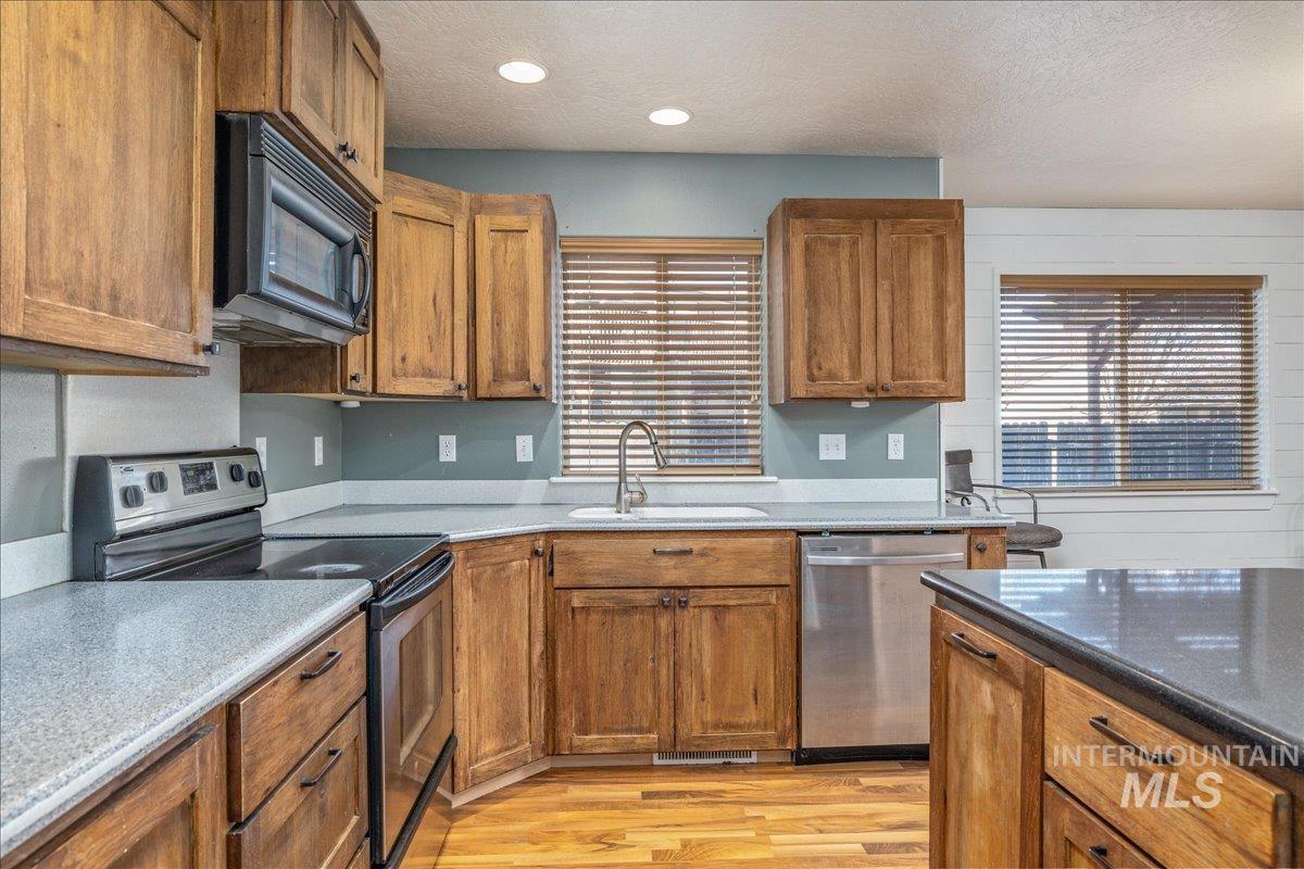 237 16th Avenue North Payette, ID 83661 - Photo 14 of 36 Kitchen featuring stainless steel appliances, brown cabinetry, light wood-type flooring, a textured ceiling, and dark stone countertops