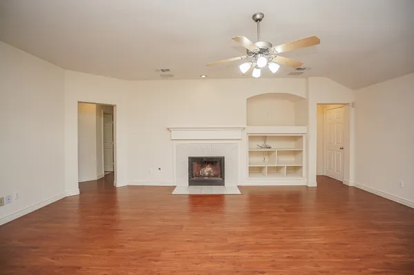 a view of an empty room with a fireplace and chandelier fan