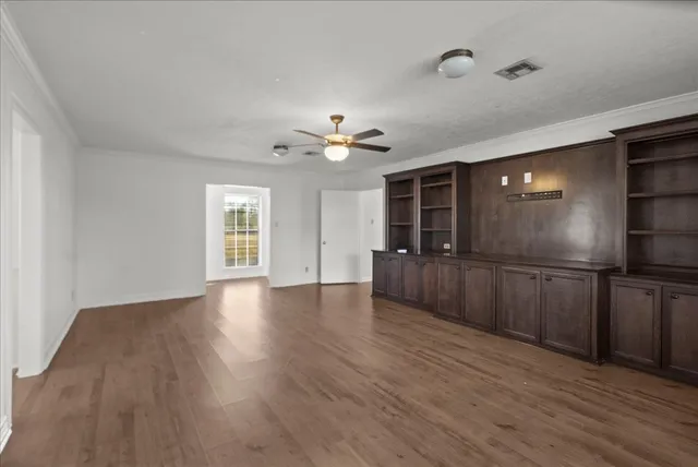 a view of an empty room with wooden floor and a kitchen