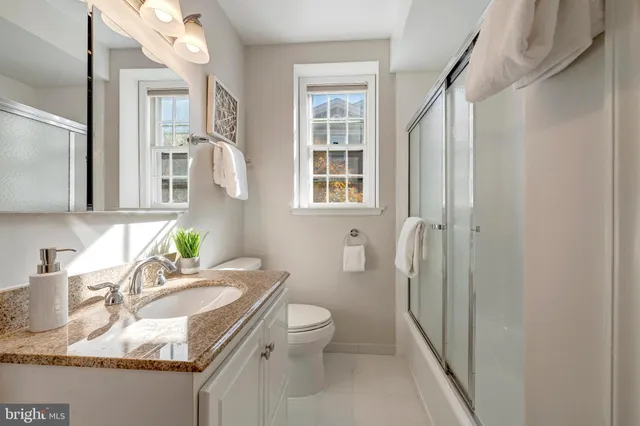 a bathroom with a granite countertop sink a mirror a toilet and a shower