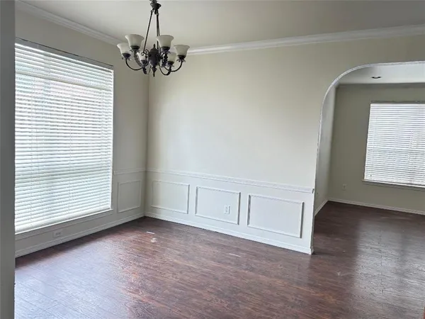 an empty room with wooden floor chandelier and windows