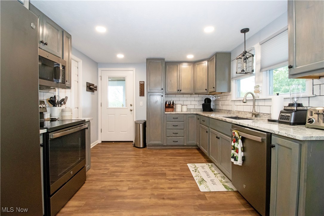 8984 Spencer Road Homerville, OH 44235 - Photo 19 of 27 Kitchen featuring appliances with stainless steel finishes, tasteful backsplash, hardwood / wood-style floors, sink, and pendant lighting