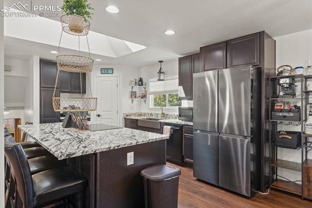28079 Iris Road Pueblo, CO 81006 - Photo 10 of 50 Kitchen featuring black appliances, a center island, dark hardwood / wood-style flooring, dark brown cabinetry, and decorative light fixtures