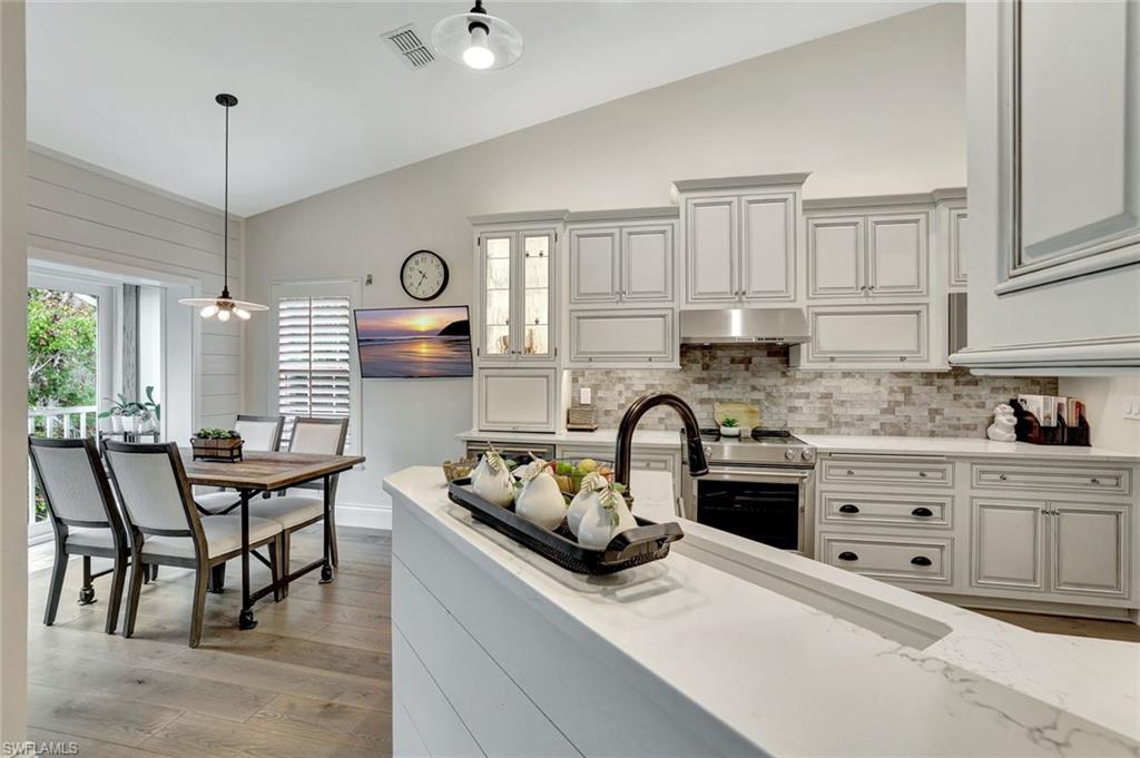 2540 Talon Court, Unit 504 Naples, FL 34105 - Photo 12 of 31 Kitchen with light stone counters, hanging light fixtures, lofted ceiling, stainless steel range, and tasteful backsplash
