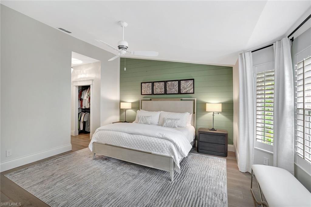 2540 Talon Court, Unit 504 Naples, FL 34105 - Photo 16 of 31 Bedroom featuring vaulted ceiling, a ceiling fan, wooden walls, wood finished floors, and a walk in closet