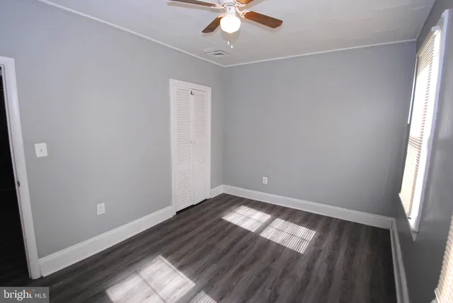 an empty room with wooden floor fan and windows