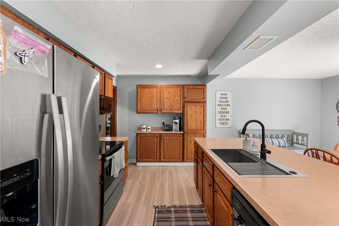 1605 Lander Road Cleveland, OH 44124 - Photo 3 of 38 Kitchen with black appliances, brown cabinetry, light countertops, a textured ceiling, and light wood-style flooring