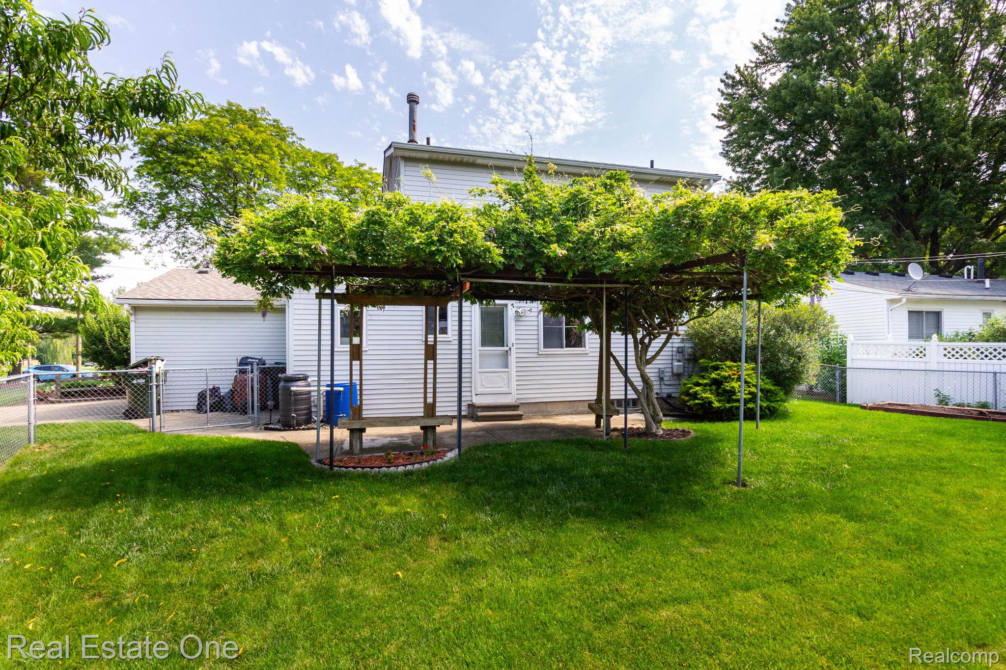 13912 Clinton River Road Sterling Heights, MI 48313 - Photo 30 of 43 Expansive backyard featuring a lush lawn, a vine-covered pergola over a patio area, and a white vinyl-sided exterior