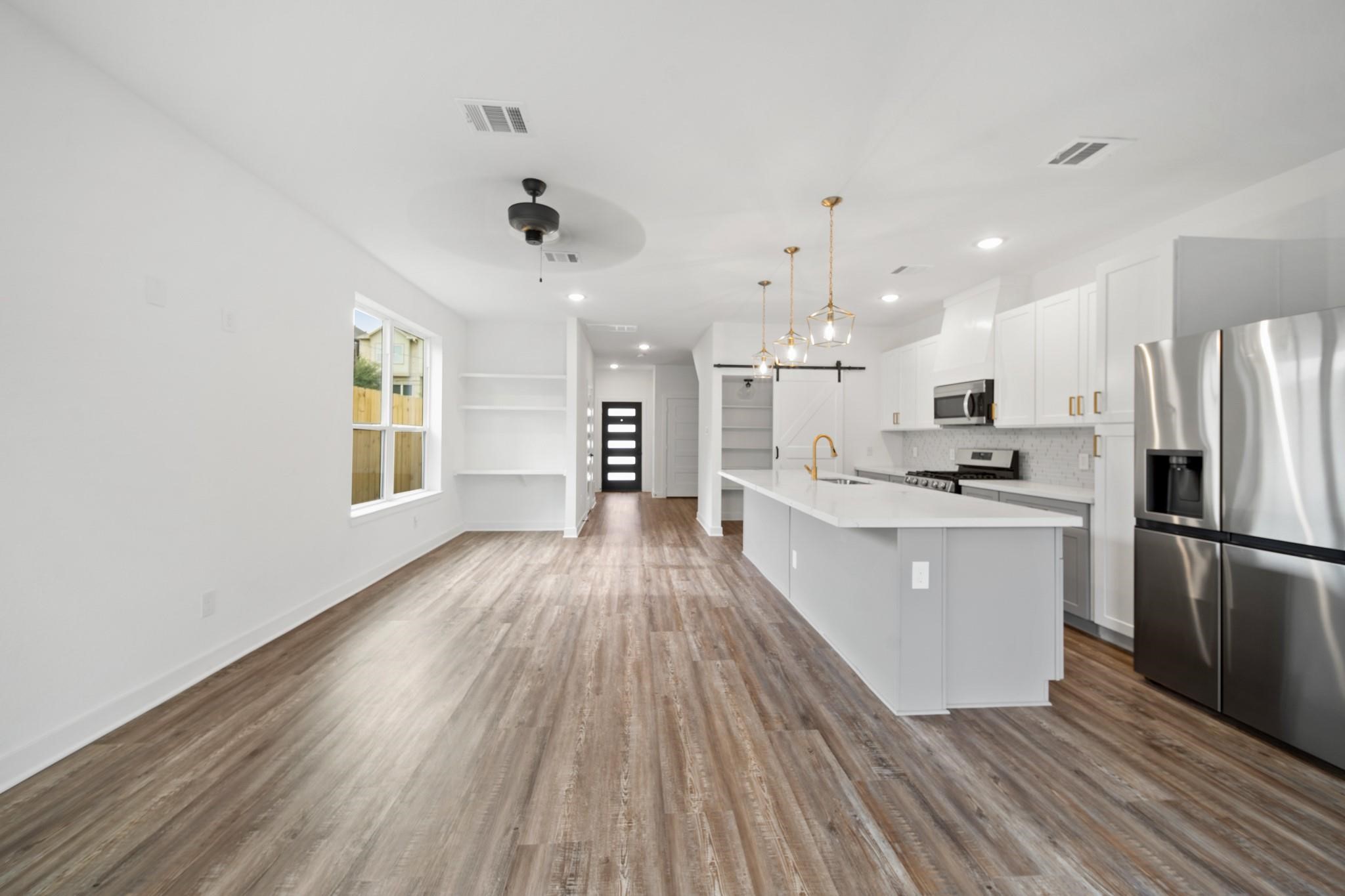 5813 England Street, Unit A Houston, TX 77021 - Photo 6 of 18 Open-concept living area with sleek hardwood floors and abundant natural light, featuring a modern kitchen with stainless steel appliances, a large island, and stylish pendant lighting.