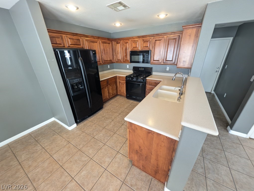9121 Spoonbill Ridge Place Las Vegas, NV 89143 - Photo 6 of 26 A functional kitchen boasts warm wood cabinetry and robust black appliances, perfect for daily living.