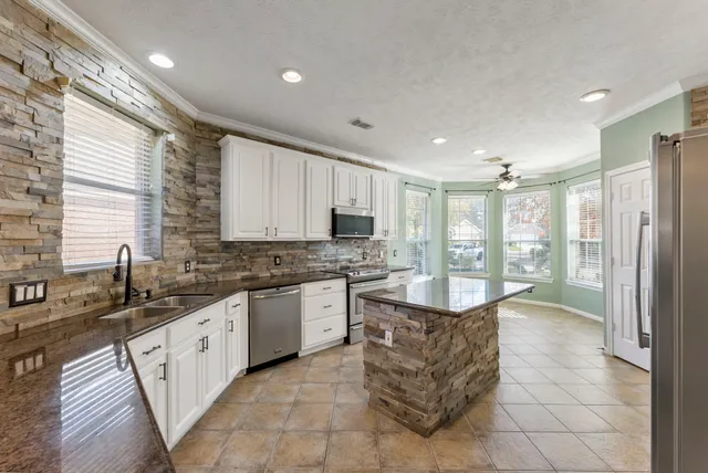 a large kitchen with kitchen island granite countertop a large counter top stainless steel appliances a sink cabinets and a window