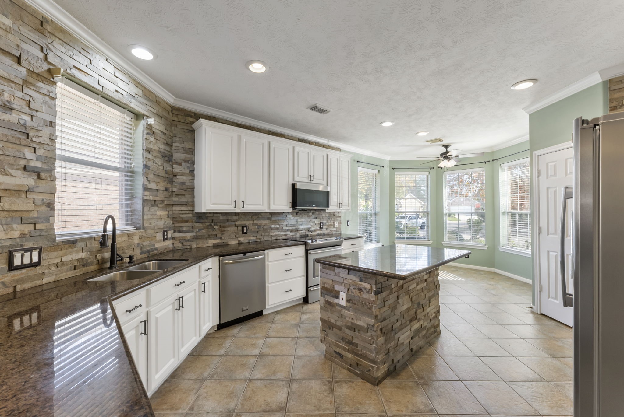 11 South Bendrook Loop Conroe, TX 77384 - Photo 3 of 27 a large kitchen with kitchen island granite countertop a large counter top stainless steel appliances a sink cabinets and a window