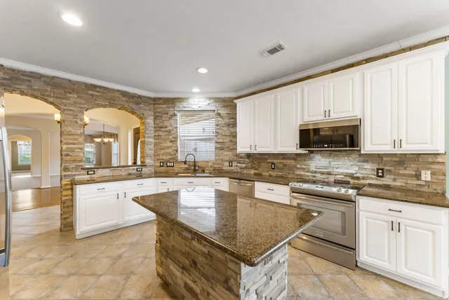 a kitchen with kitchen island granite countertop a stove a sink dishwasher and white cabinets with wooden floor