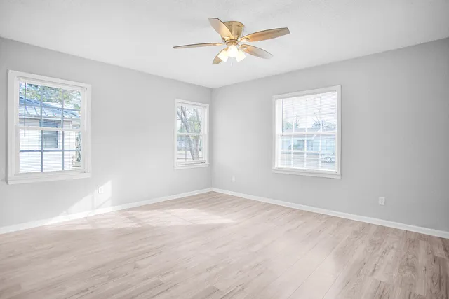 an empty room with wooden floor fan and windows