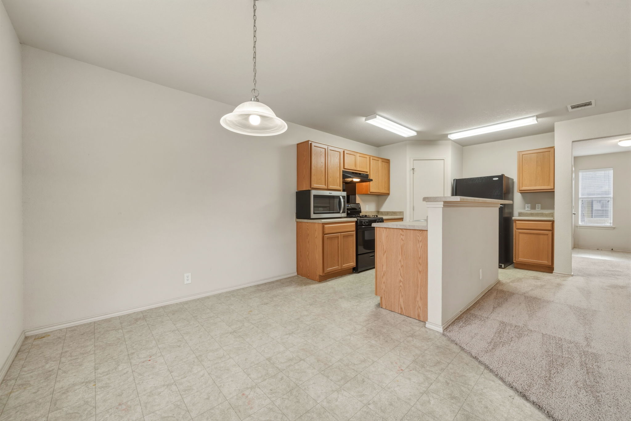 4528 Best Way Austin, TX 78725 - Photo 13 of 40 Kitchen featuring light countertops, hanging light fixtures, black appliances, light flooring, and a kitchen island