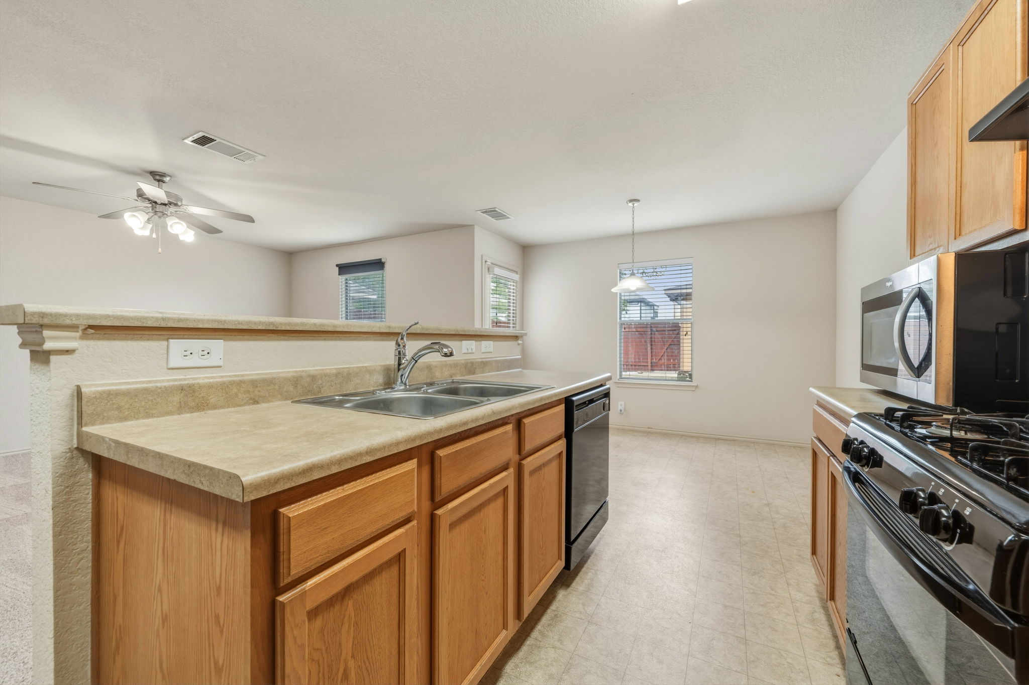4528 Best Way Austin, TX 78725 - Photo 18 of 40 Kitchen featuring light countertops, light floors, black dishwasher, a center island with sink, and hanging light fixtures