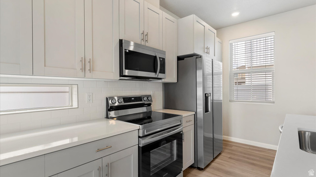 82 Provo River Road, Unit 251 Saratoga Springs, UT 84045 - Photo 12 of 32 Kitchen featuring light-toned upper cabinetry, stainless steel appliances, a subway tile backsplash, light-toned countertops, and wood-finish flooring