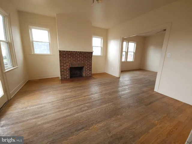 a view of an empty room with wooden floor fireplace and a window