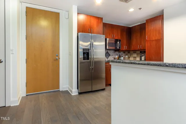 a kitchen with stainless steel appliances granite countertop a refrigerator a sink a stove a microwave and island with wooden floor