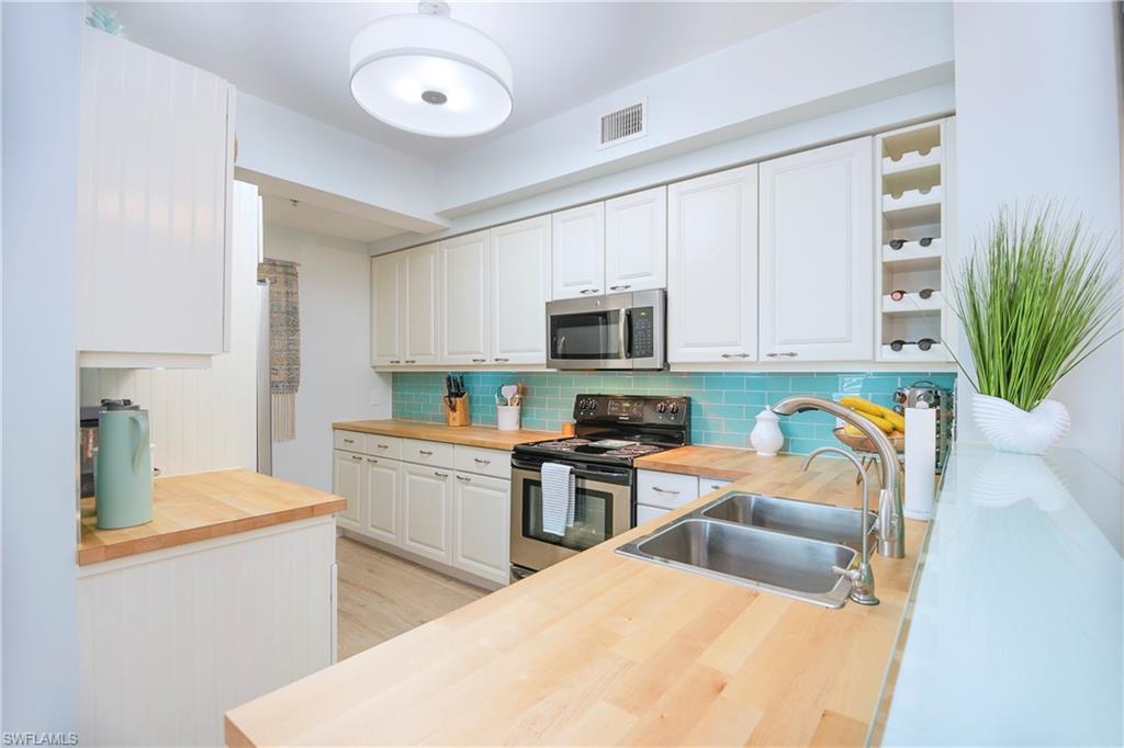 1160 Reserve Way, Unit 303 Naples, FL 34105 - Photo 2 of 19 a kitchen with stainless steel appliances a stove a sink a refrigerator white cabinets and wooden floor