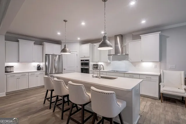 a large white kitchen with a refrigerator a stove a sink dishwasher a dining table and chairs with wooden floor