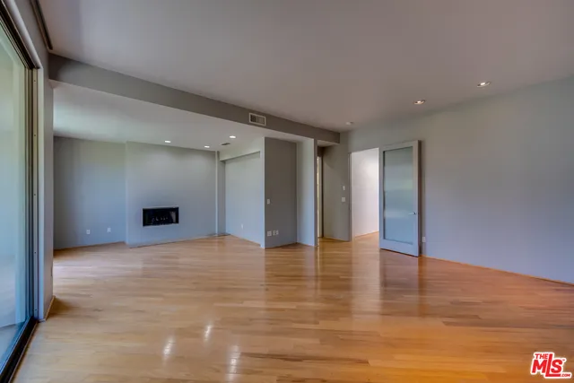 a view of an empty room with wooden floor and kitchen