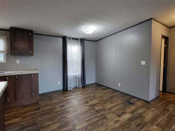a view of an empty room with wooden floor and a kitchen