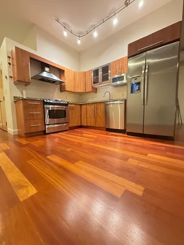 a view of kitchen with stainless steel appliances wooden floor and living room