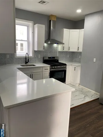 a kitchen with stainless steel appliances a sink dishwasher a stove and white cabinets with wooden floor