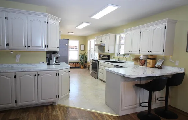 a kitchen with stainless steel appliances granite countertop a sink dishwasher stove and white cabinets with wooden floor