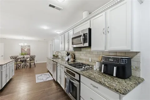 a kitchen with stainless steel appliances granite countertop a stove top oven a sink a dining table and chairs with wooden floor