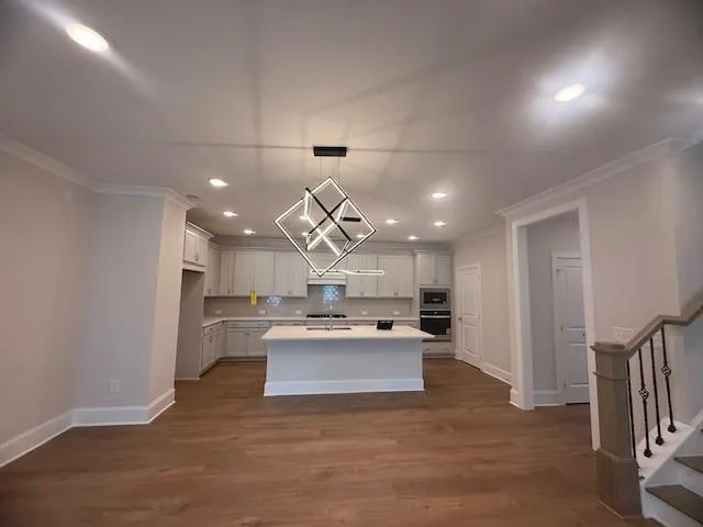 a large kitchen with kitchen island a stove a sink dishwasher a refrigerator and white cabinets with wooden floor