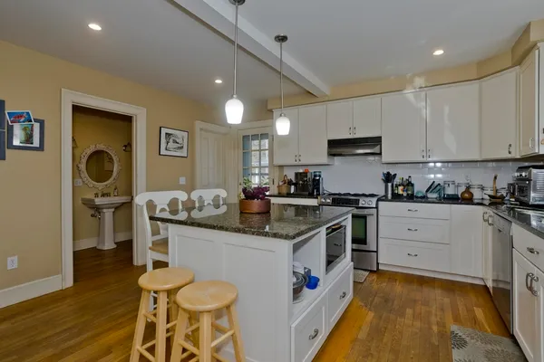 a kitchen with stainless steel appliances granite countertop a stove top oven a sink dishwasher and white cabinets with wooden floor