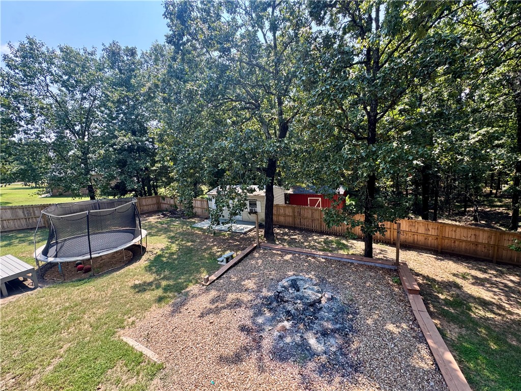 1197 Ridgeview Lane Russellville, AR 72802 - Photo 35 of 44 Expansive backyard featuring a gravel fire pit area, mature trees providing natural shade, a privacy fence, a storage shed, and a wooden bench