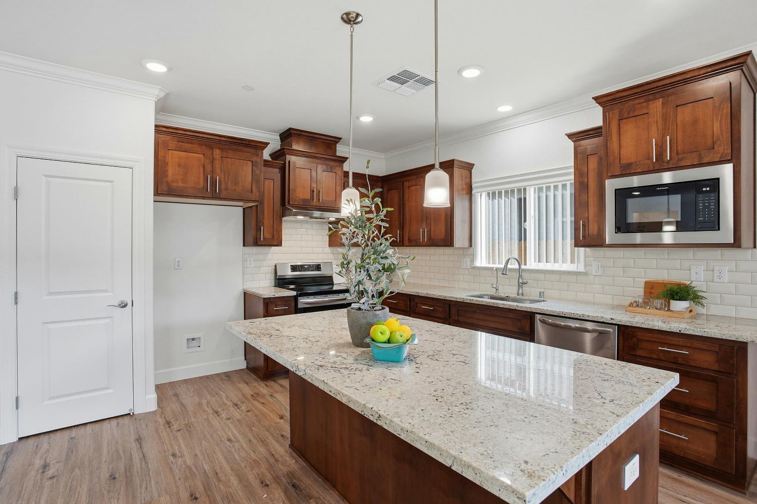 1112 Audrey Court Galt, CA 95632 - Photo 2 of 37 a kitchen with granite countertop a stove a kitchen island a sink dishwasher and a wooden cabinets
