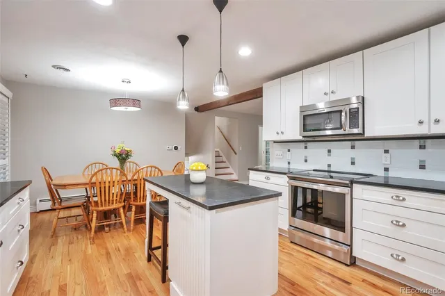 a kitchen with stainless steel appliances granite countertop a stove a sink a dining table and chairs with wooden floor