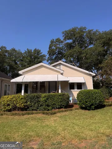 a view of a white house with a yard plants and large tree