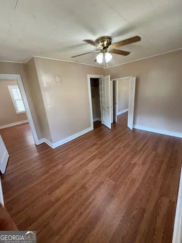 a view of an empty room with wooden floor and a ceiling fan
